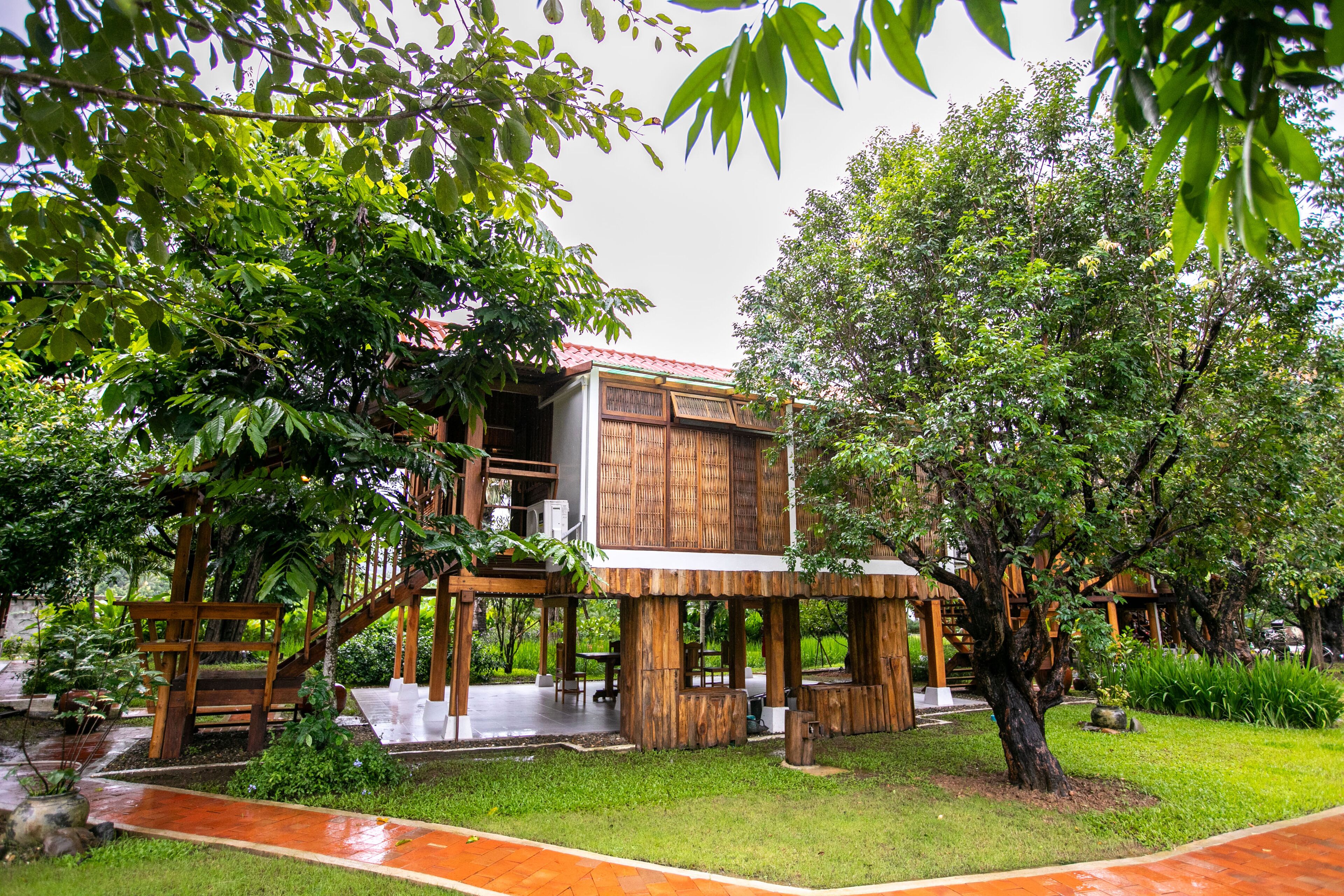 A wooden structure with a red roof, surrounded by lush greenery and a paved walkway.