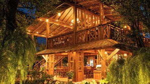 A wooden cabin with a deck and outdoor seating area surrounded by lush greenery.