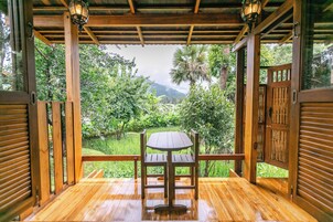 Une terrasse en bois avec une table et des chaises, offrant une vue sur un jardin luxuriant et sur les montagnes.