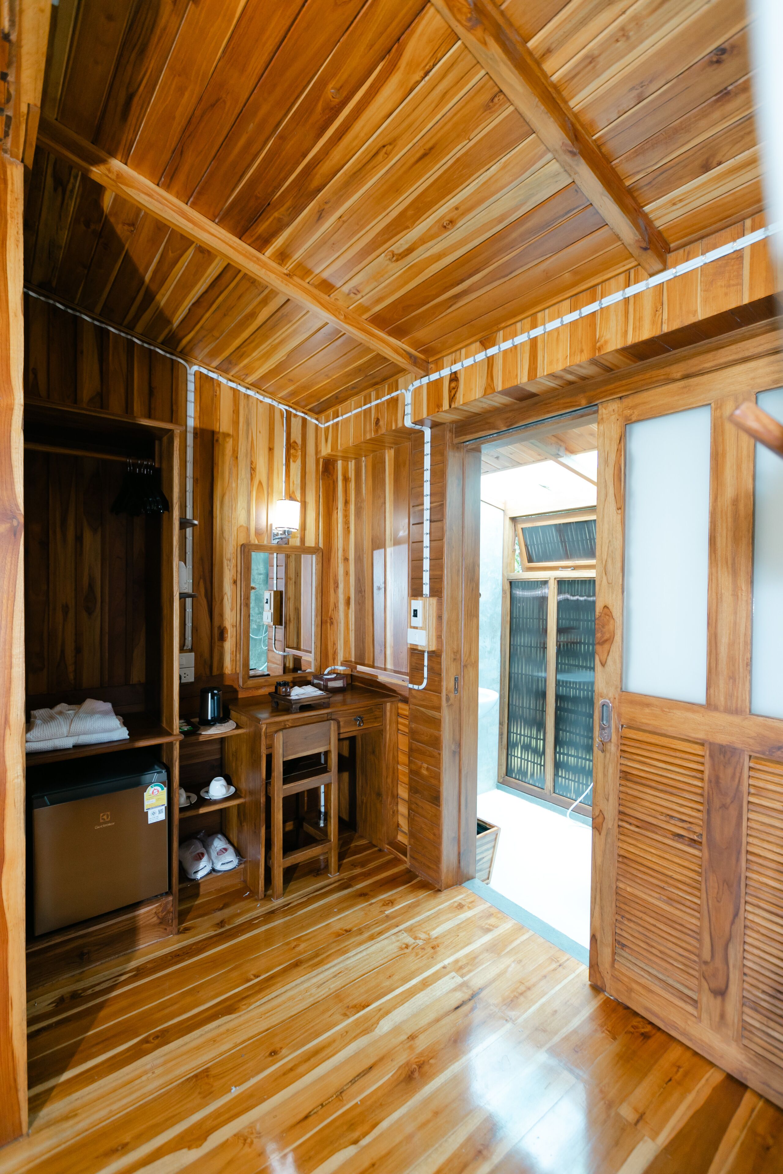 A wooden interior with a wooden floor, a sink, a mirror, and a door leading outside.