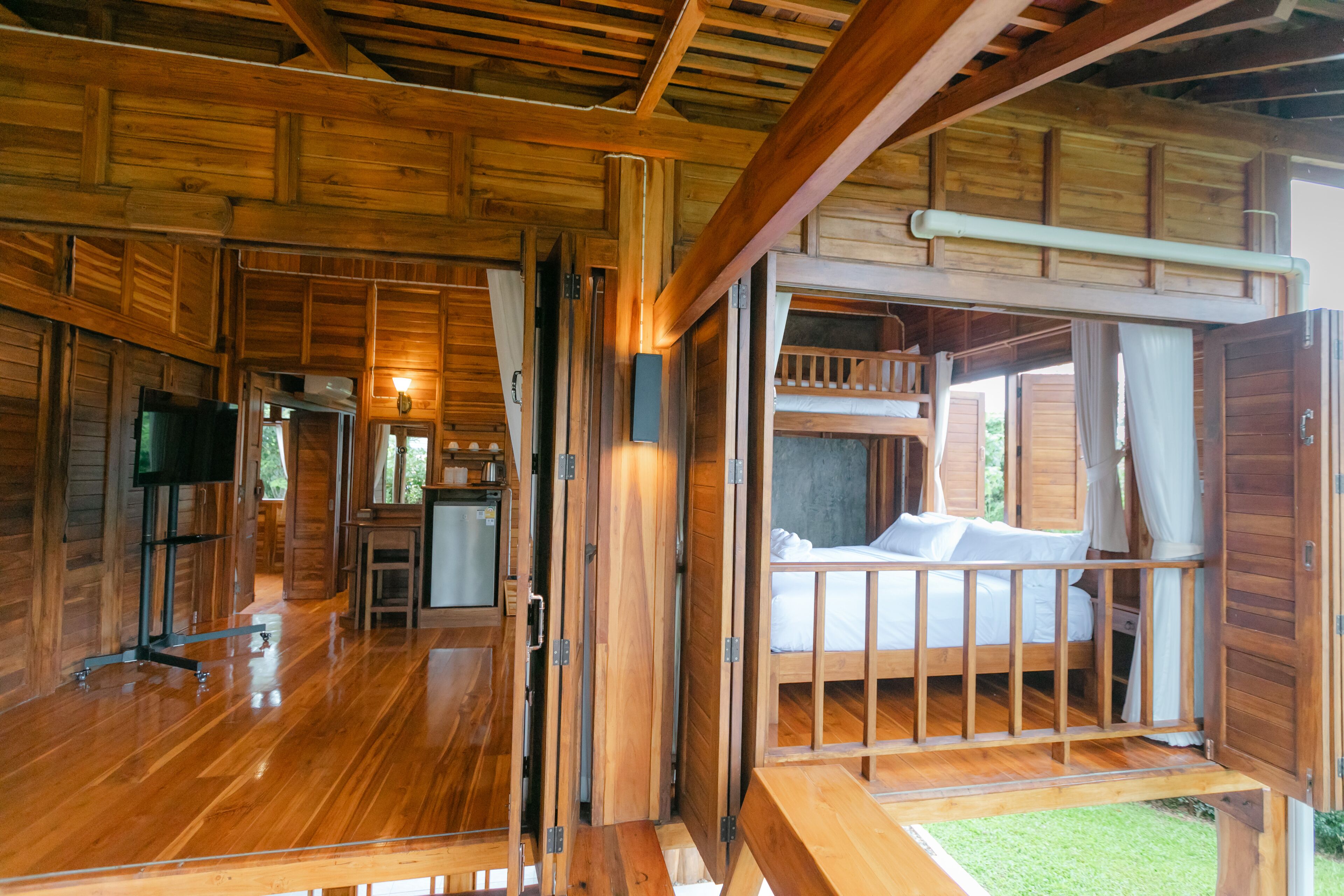 A wooden cabin interior with a kitchen area, a dining table, and a bed with a balcony.