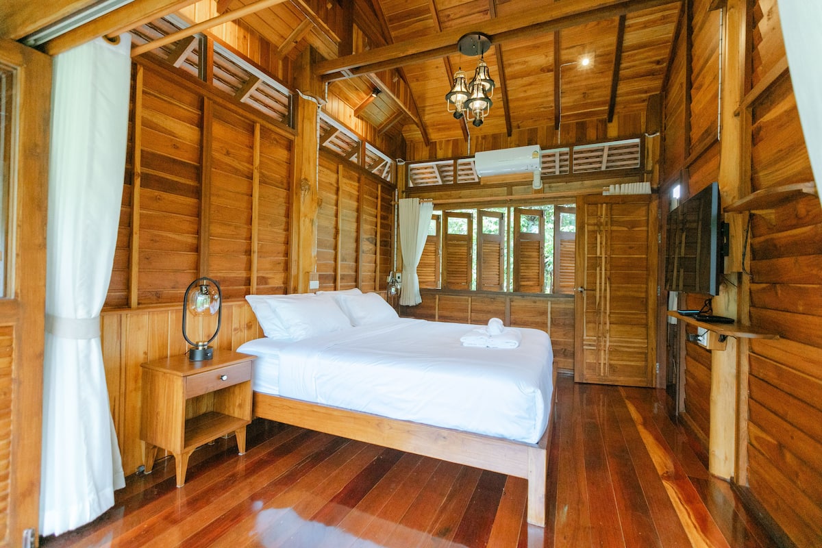 A wooden cabin bedroom with a bed, nightstand, lamp, and a ceiling fan.