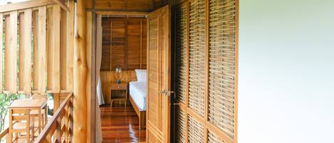 A wooden corridor with a wooden floor, a bed with a white mattress, a nightstand with a mirror, and a hanging light fixture.