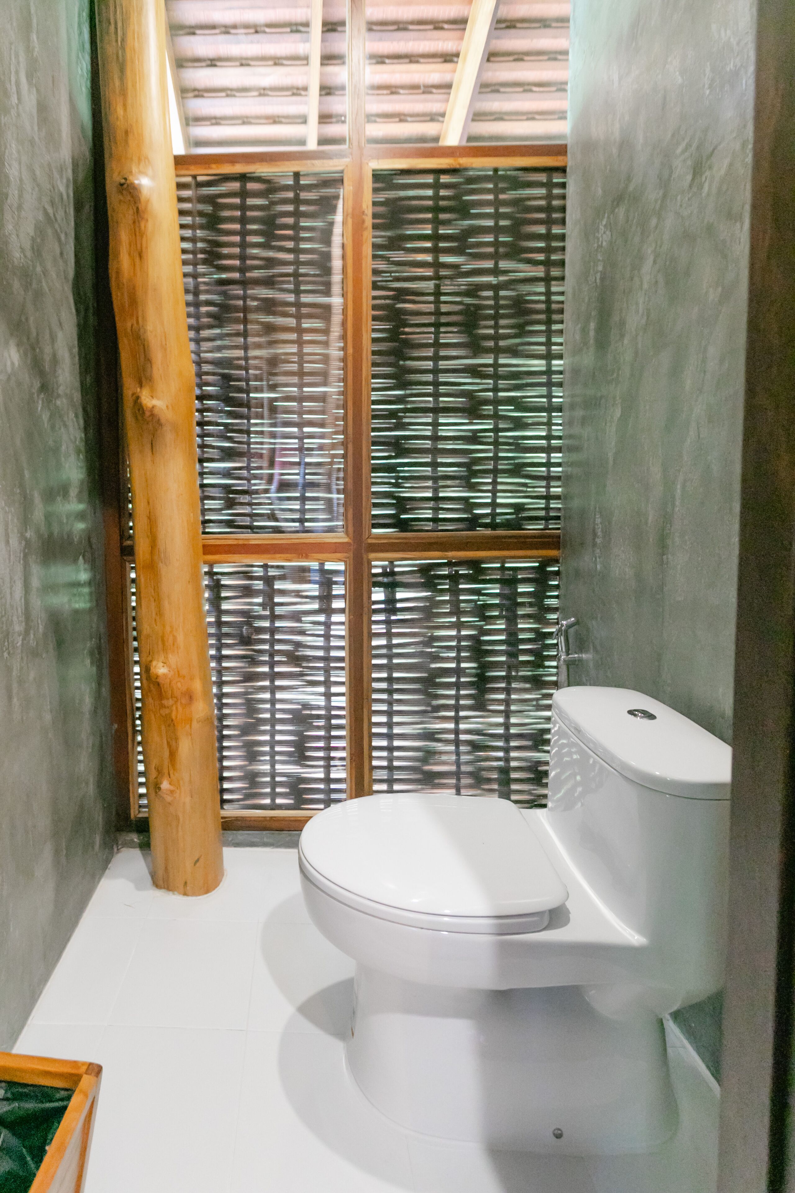 A compact bathroom with a white toilet, a wooden column, and a bamboo screen door.