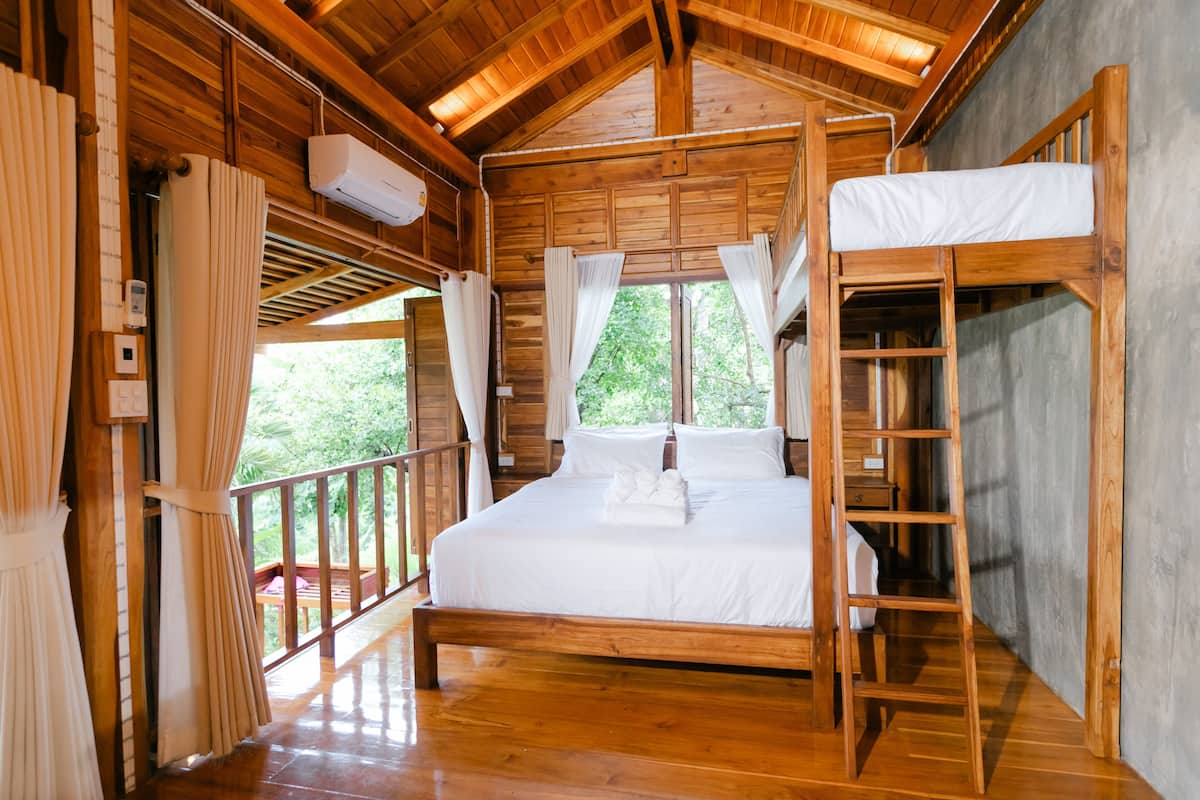 A wooden cabin with a bunk bed, a wooden ladder, and a balcony with curtains.