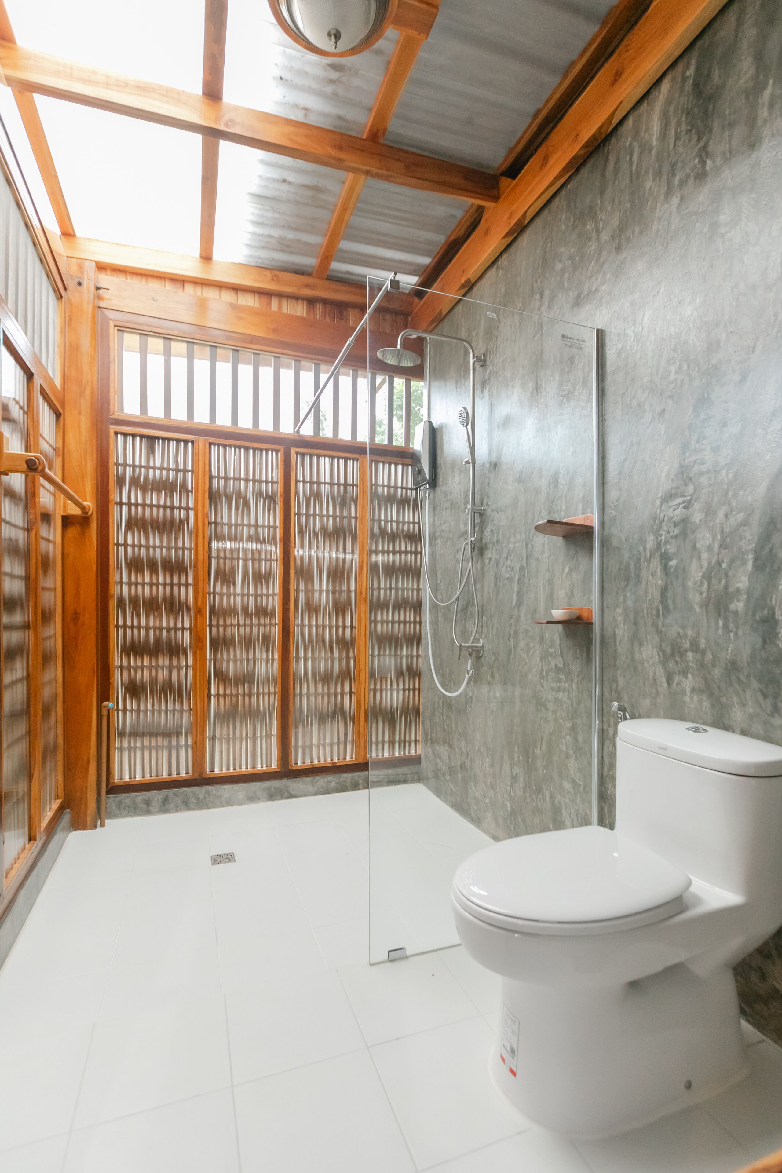 A bathroom with a wooden ceiling, a shower, a toilet, and a large window with a view.