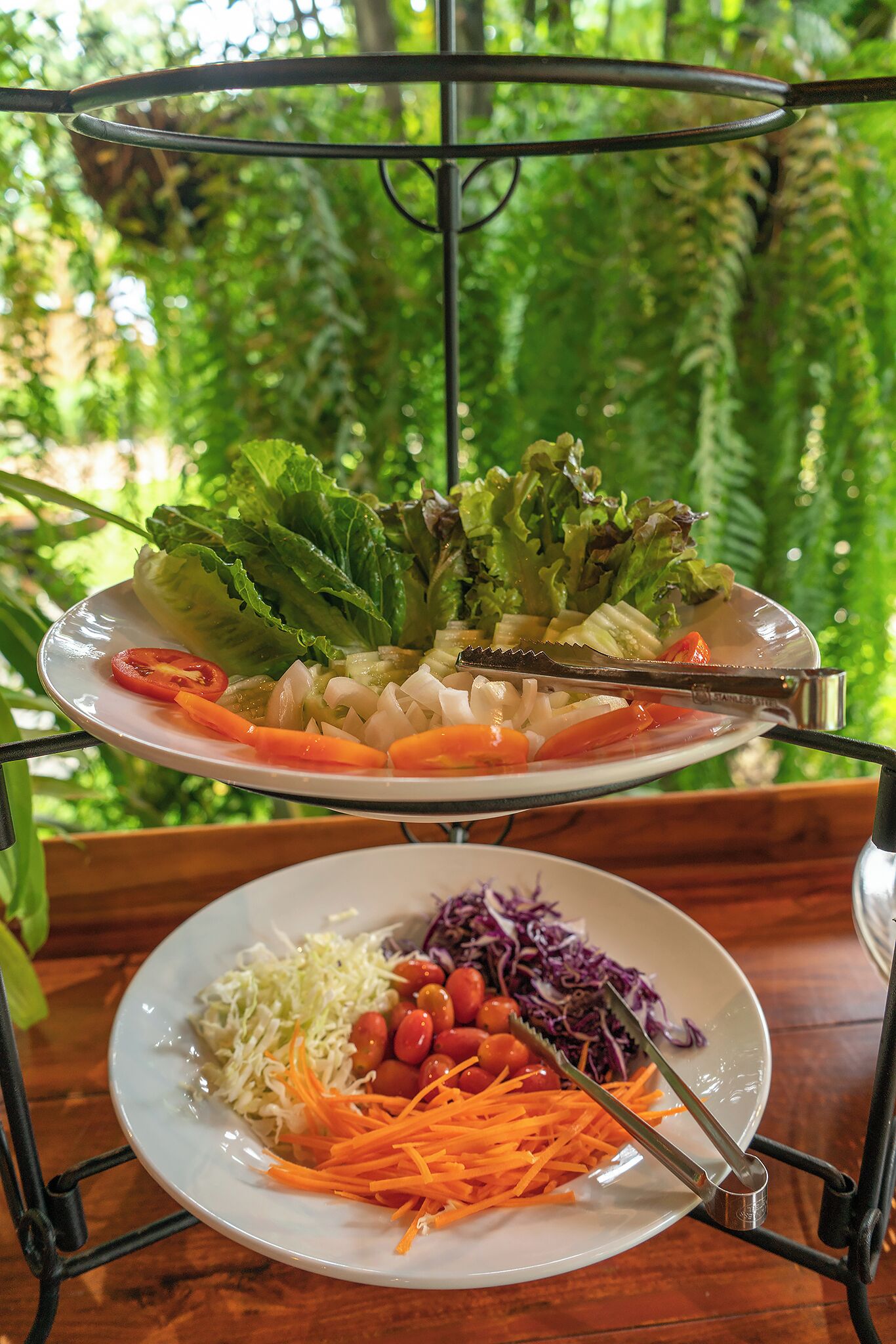 A salad on a metal stand with a plate of vegetables and a plate of shredded carrots and cabbage.