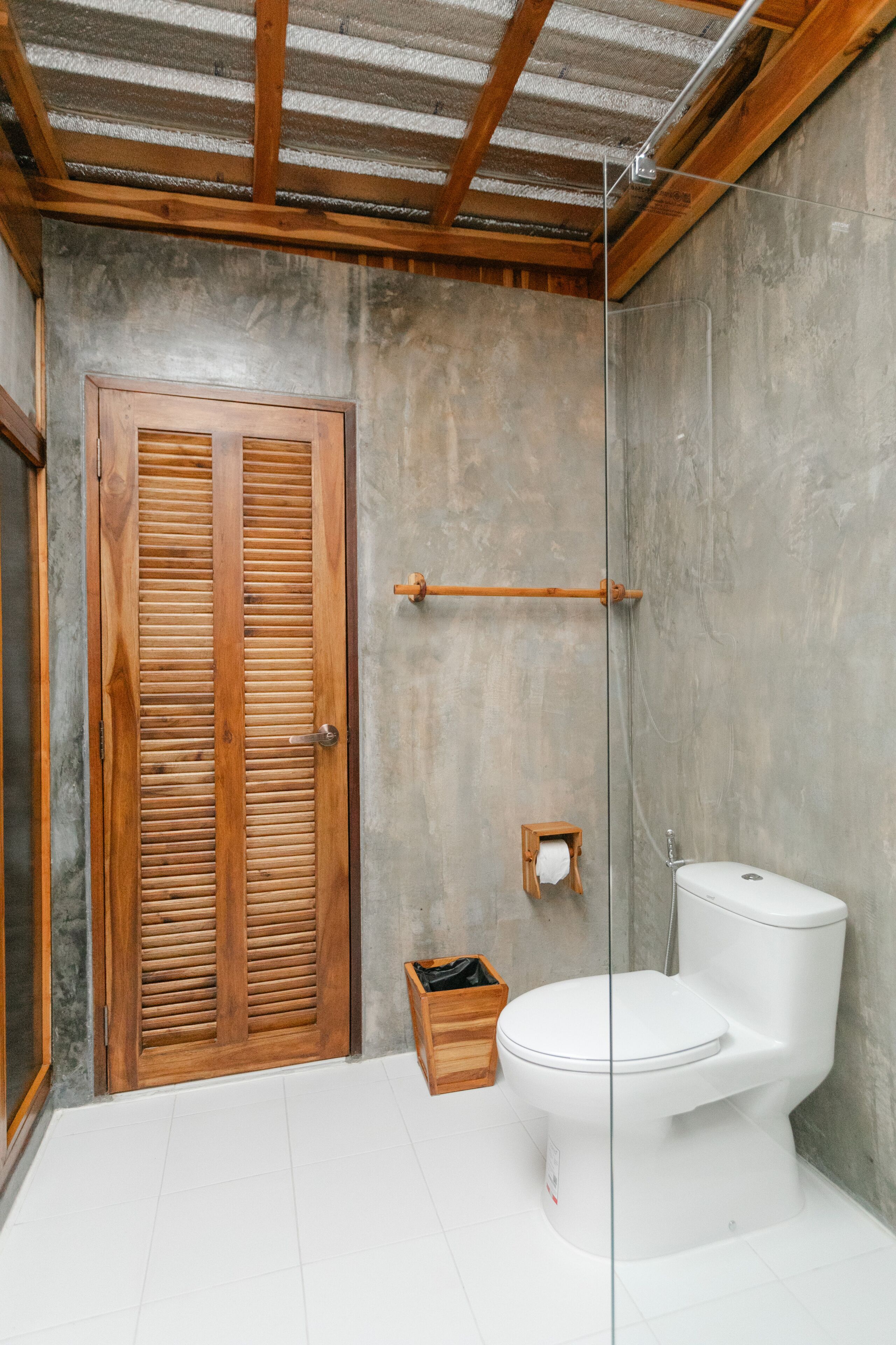 A bathroom with a wooden door, a white toilet, and a concrete wall.