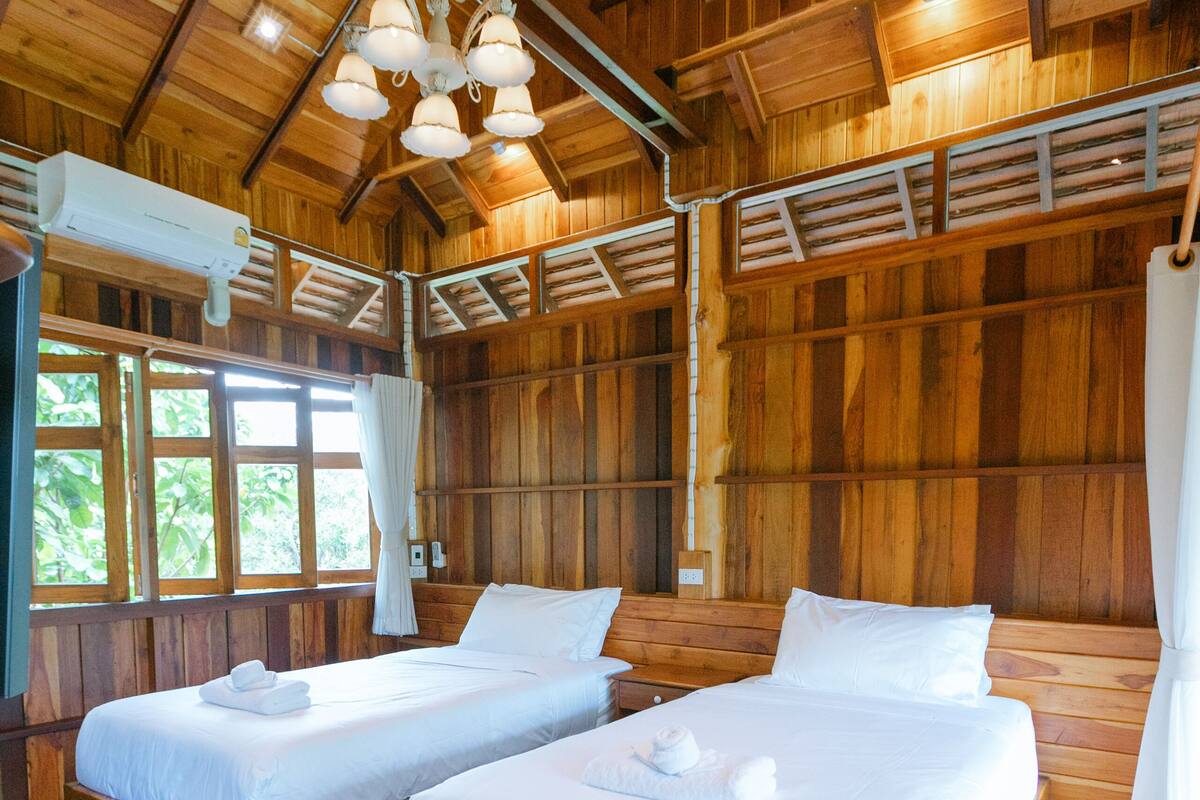 A wooden cabin with two wooden beds, a ceiling fan, and a large window with curtains.