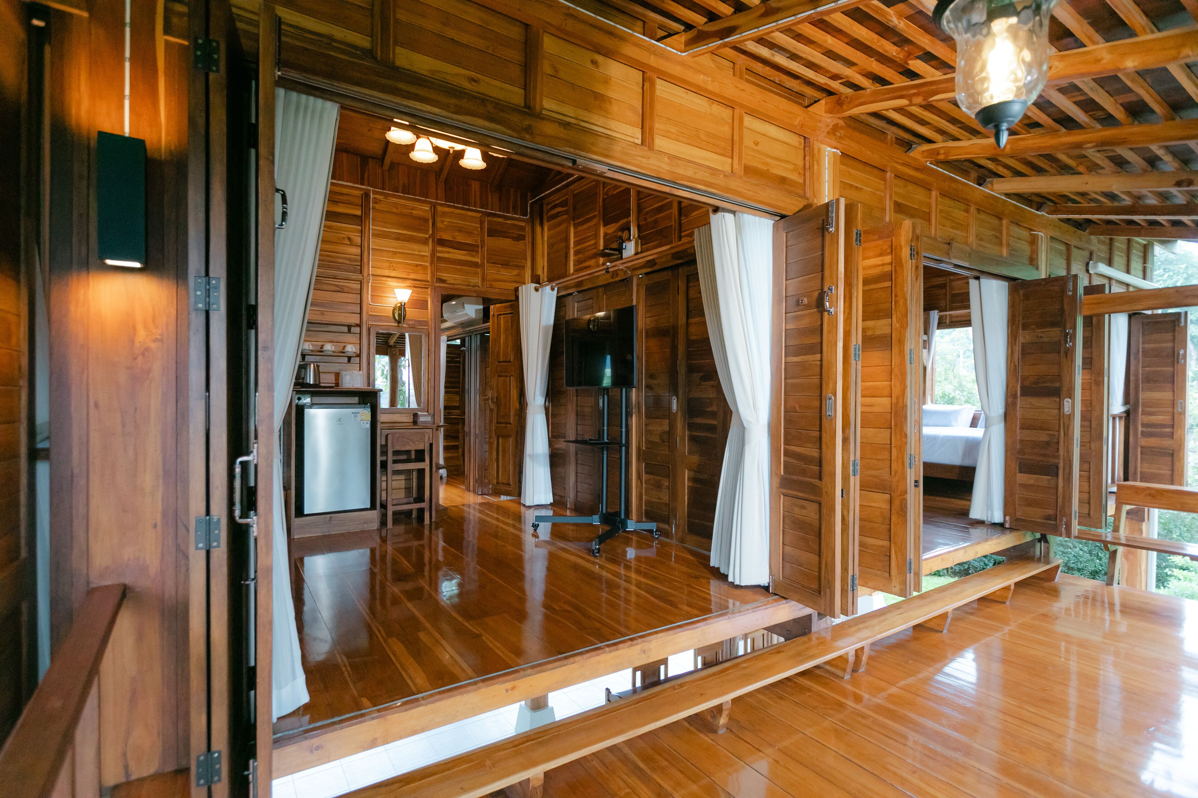 Interior de una cabaña de madera con suelo de madera, televisor, pequeña cocina y puerta corrediza.