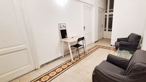 Un pasillo con un sofá, una mesita y una silla. Se ve una puerta al final del pasillo.