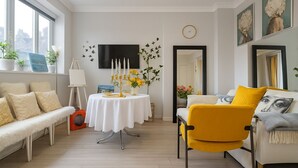 Un salón moderno con un sofá, un sillón amarillo, una mesa de comedor con mantel blanco y un televisor de pantalla plana montado en la pared.