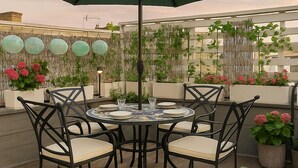 Una terraza en la azotea con una mesa redonda, sillas y una sombrilla.