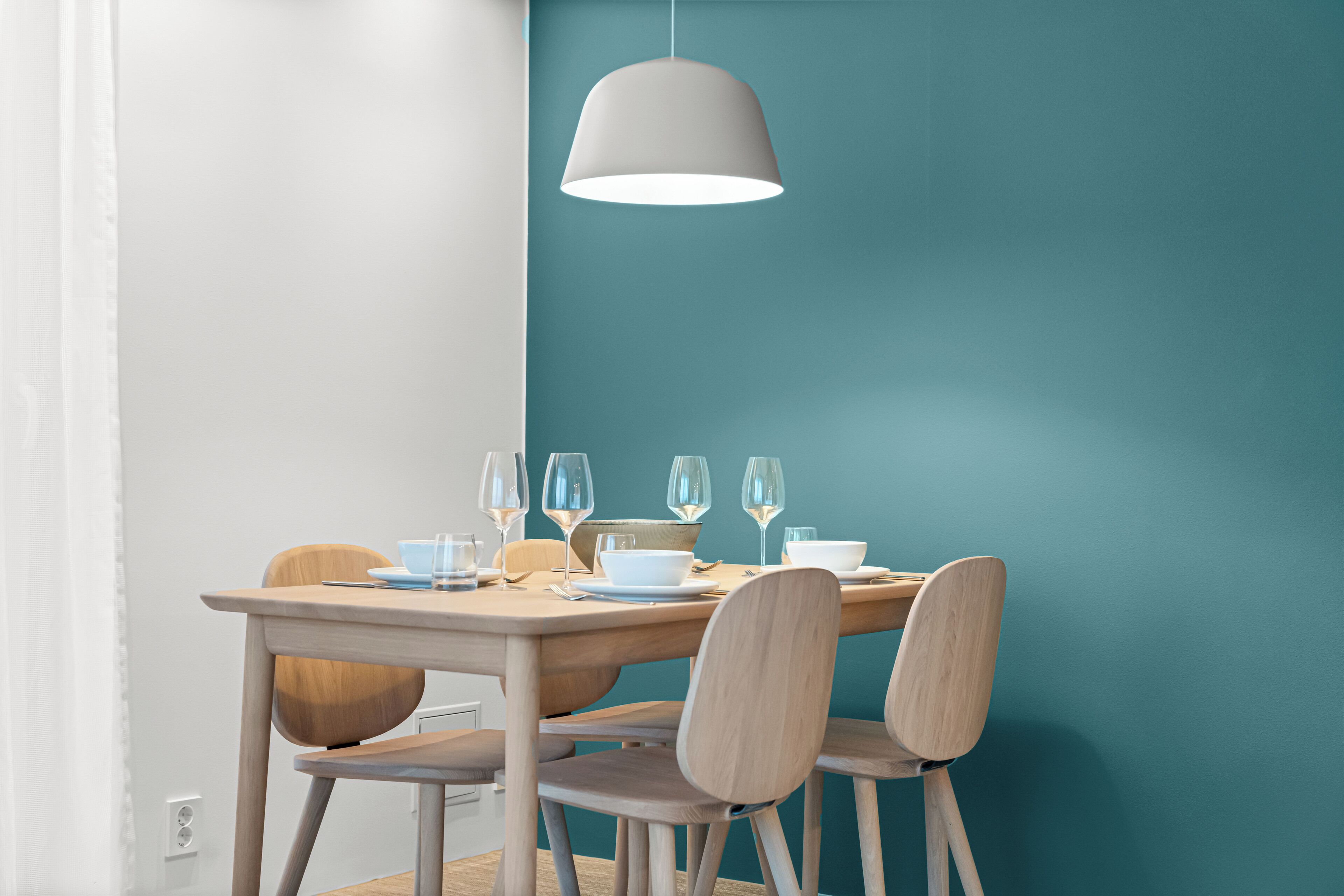 A dining area with a table set for four, a hanging light fixture, and teal-colored walls.