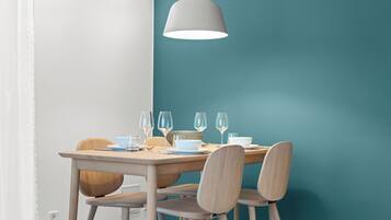 A dining area with a table set for four, a hanging light fixture, and teal-colored walls.