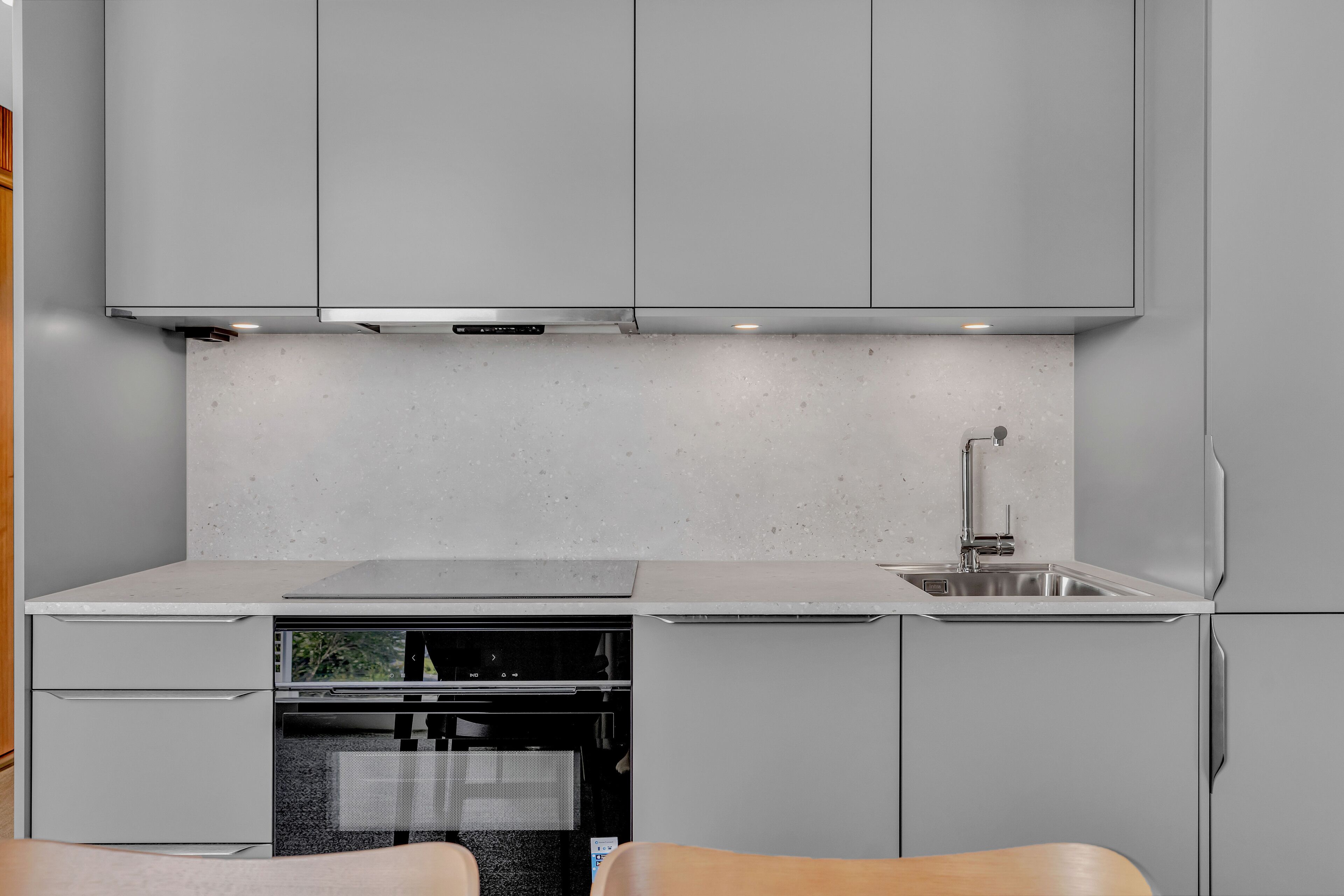 A modern kitchen with grey cabinets, a stainless steel sink, and a built-in oven.