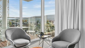 Una habitación moderna con dos sillones grises, una mesita y un ventanal grande que ofrece vistas a la ciudad.