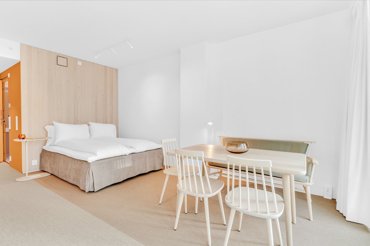 Una habitación de hotel moderna con cama, mesita de noche y un área de comedor con sillas y una mesa.