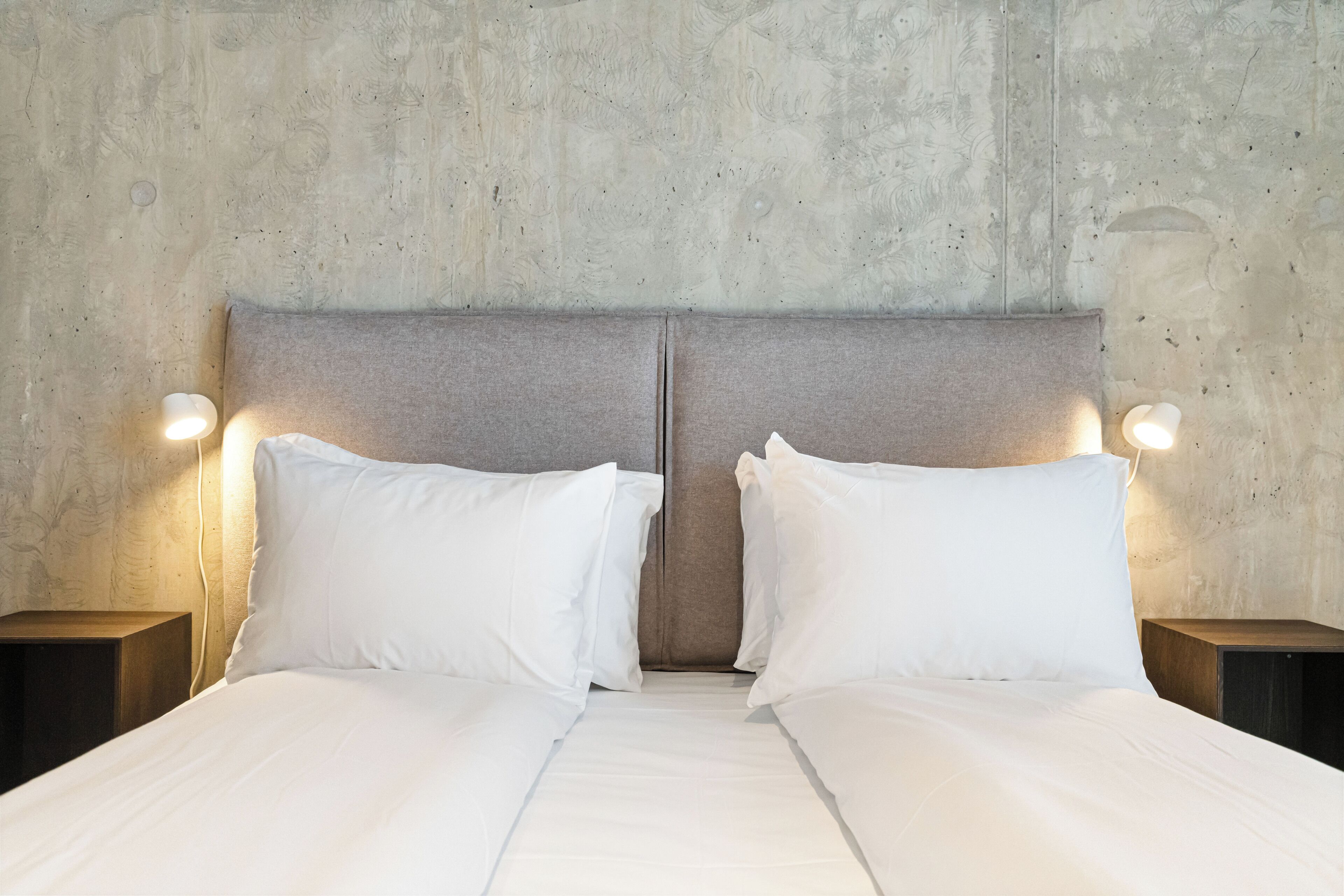 A double bed with white linens and two nightstands with wall-mounted lamps.