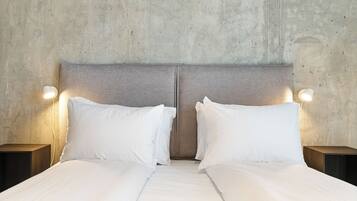 A double bed with white linens and two nightstands with wall-mounted lamps.