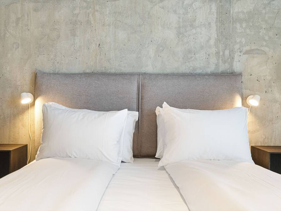 A double bed with white linens and two nightstands with wall-mounted lamps.