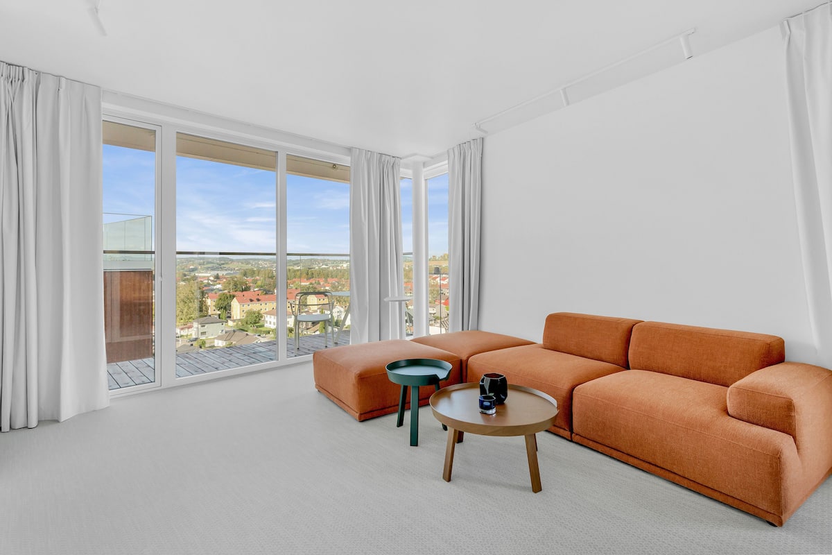 Una sala de estar moderna con un ventanal grande, un sofá modular, una mesita redonda y una silla verde.