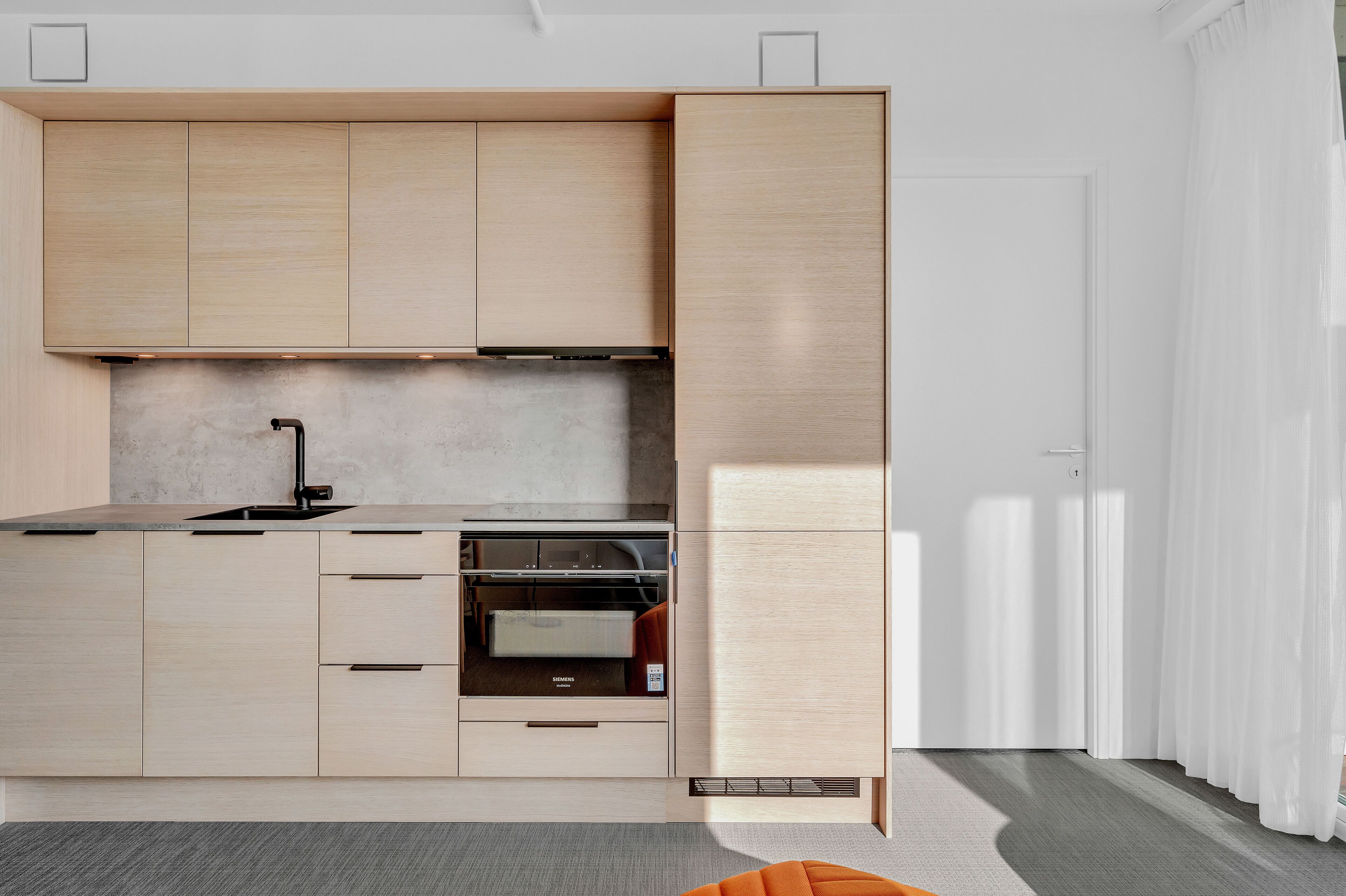 Une cuisine moderne avec des meubles de couleur bois clair, un four encastré et un robinet noir élégant.