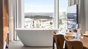 Un baño moderno con una bañera independiente, un comedor con una mesa para dos personas y un ventanal que ofrece vistas a un paisaje urbano.