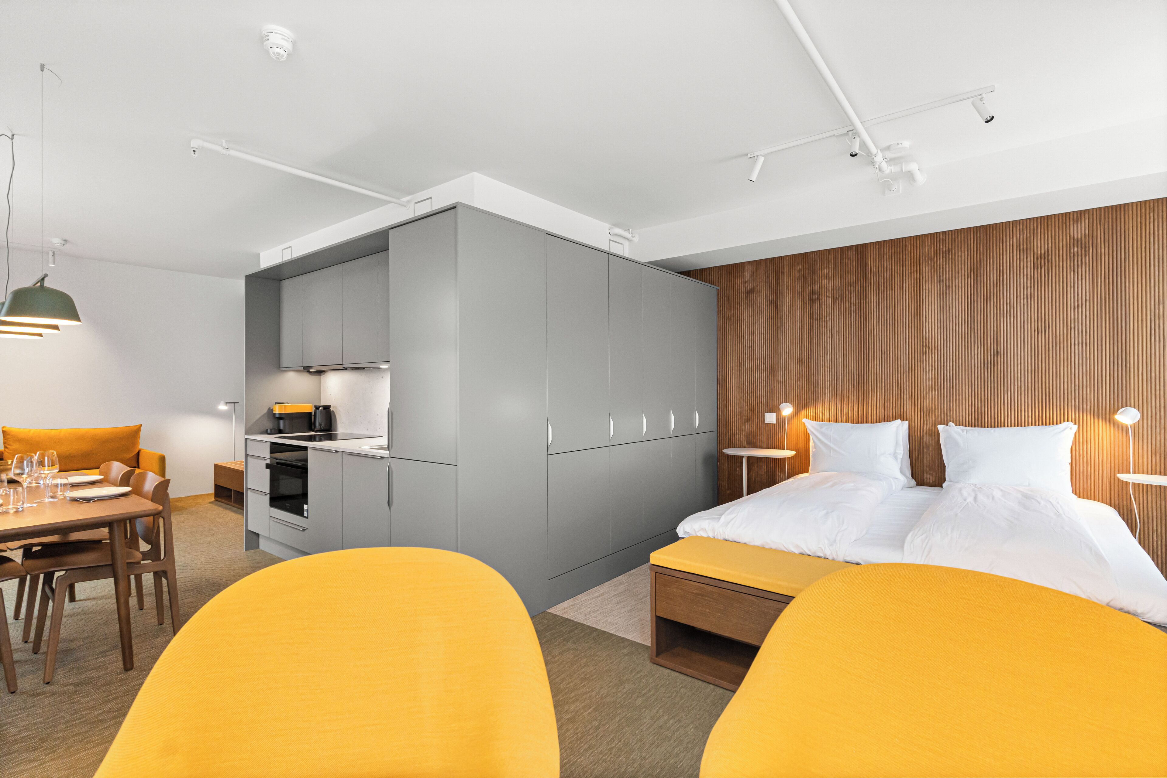 A modern hotel room with a kitchenette, a dining area, and a large bed with a wooden headboard.
