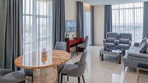 Una sala de estar moderna con una mesa redonda, dos sillones grises, un sofá y un televisor montado en la pared.