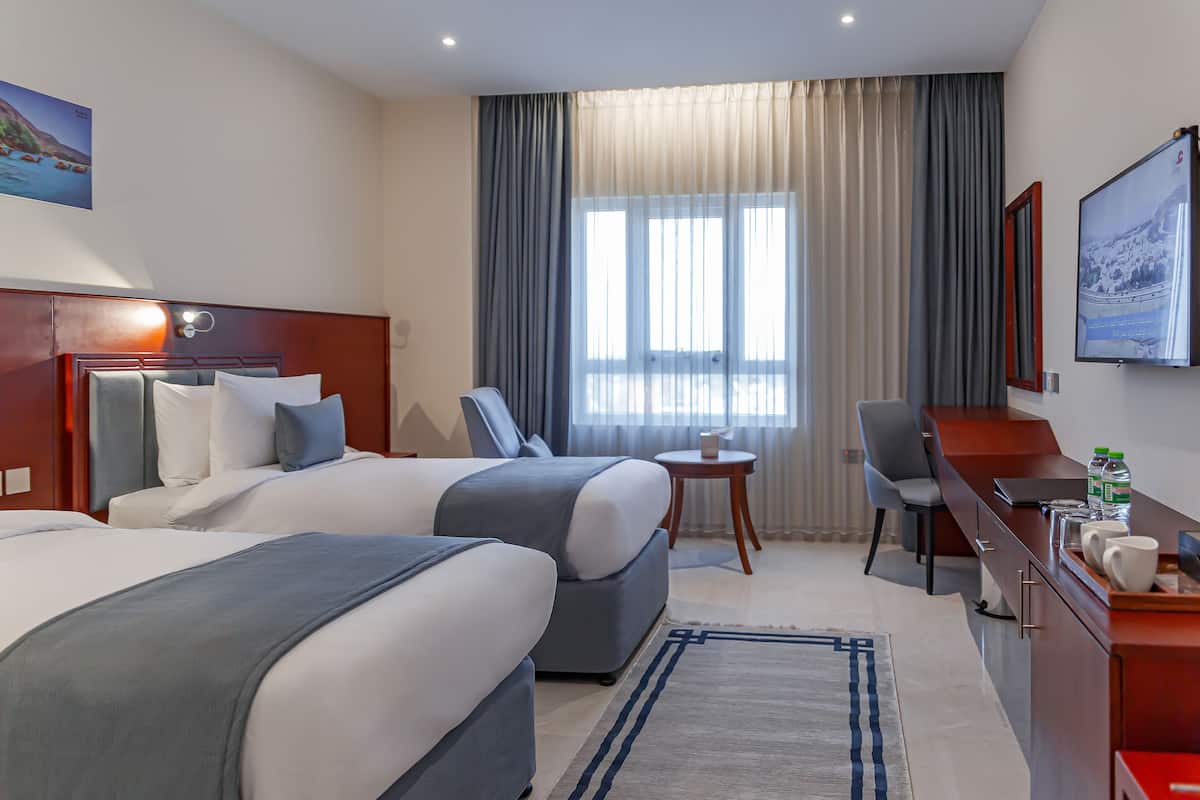 Habitación de hotel con dos camas, un escritorio, una silla, una mesita y un televisor.