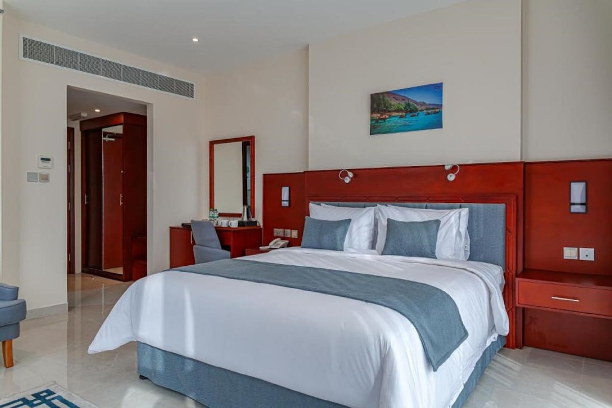 Une chambre d’hôtel avec un grand lit, un bureau avec une chaise, un miroir et un tableau au mur.