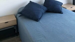 Makuuhuoneessa on sänky, kaksi tyynyä, yöpöytä ja seinälle ripustettu taideteos, jossa on kuvattuna puinen laituri.