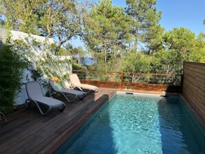 A pool area with two lounge chairs and a wooden deck.