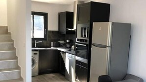 Moderni keittiö, jossa on sisäänrakennettu uuni, jääkaappi sekä ruokailutila pöytineen ja tuoleineen.