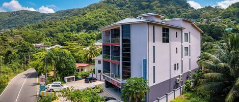 A multi-story hotel with a modern design, located in a lush, green area with a mountain backdrop.