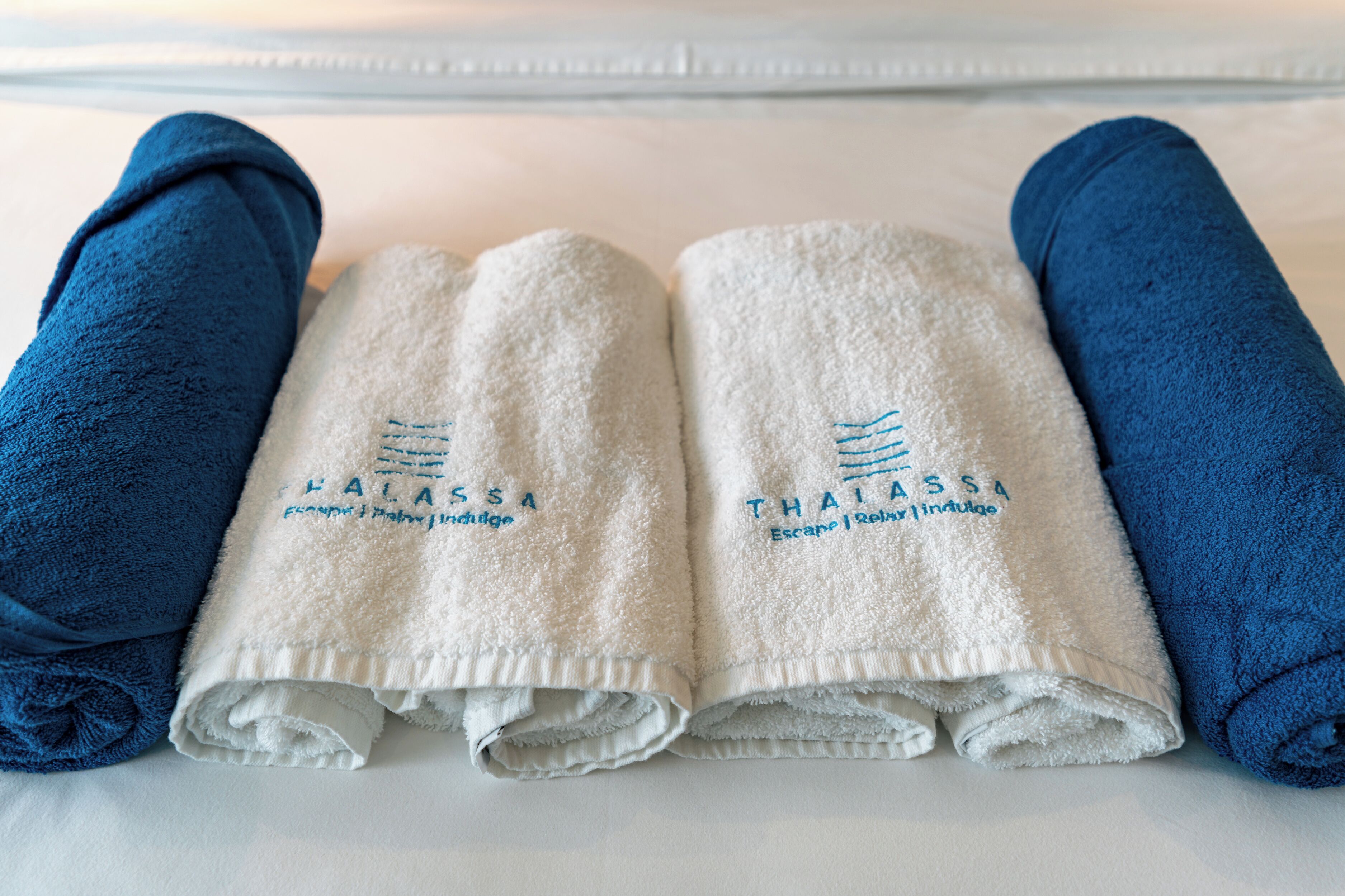A neatly arranged set of towels on a bed, with two blue towels on the sides and two white towels in the center, each with embroidered text.