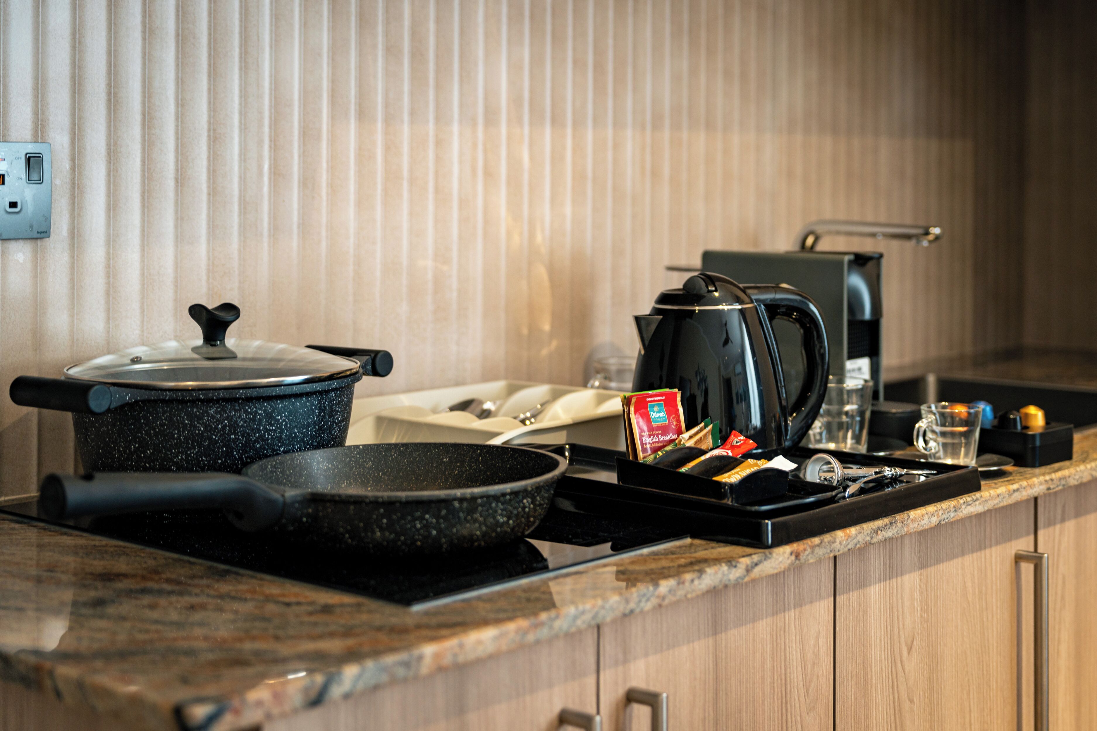 A kitchen with a stove, a frying pan, a pot, a kettle, and a coffee maker.