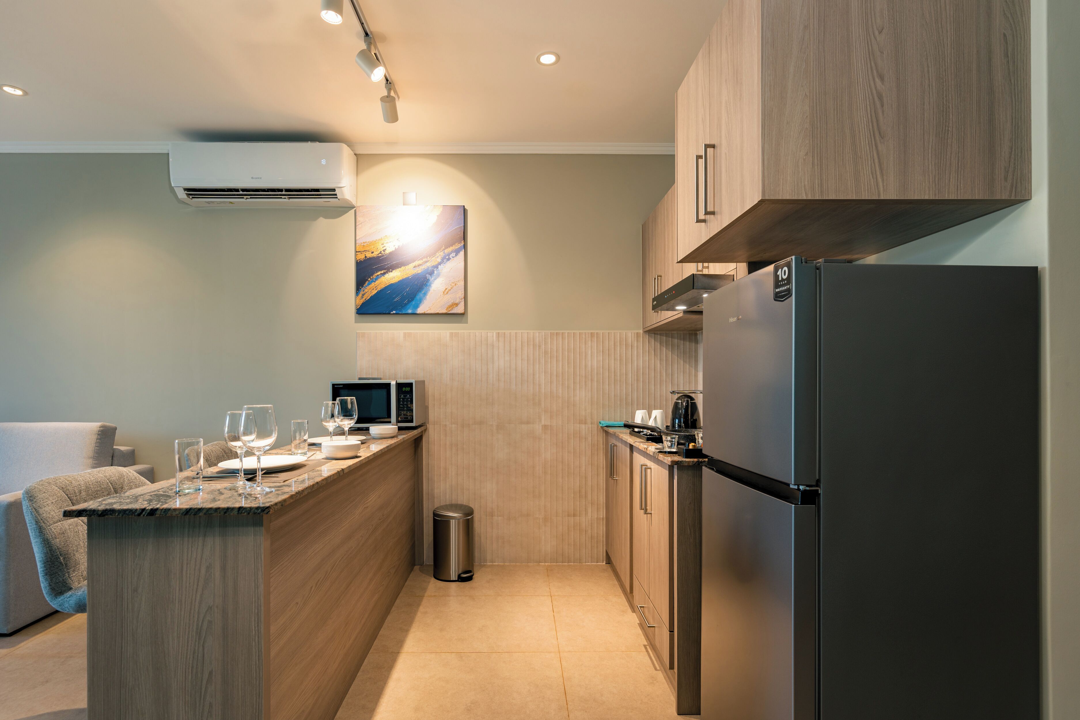 Une cuisine moderne avec des meubles en bois, un réfrigérateur en acier inoxydable, un four à micro-ondes et une poubelle.