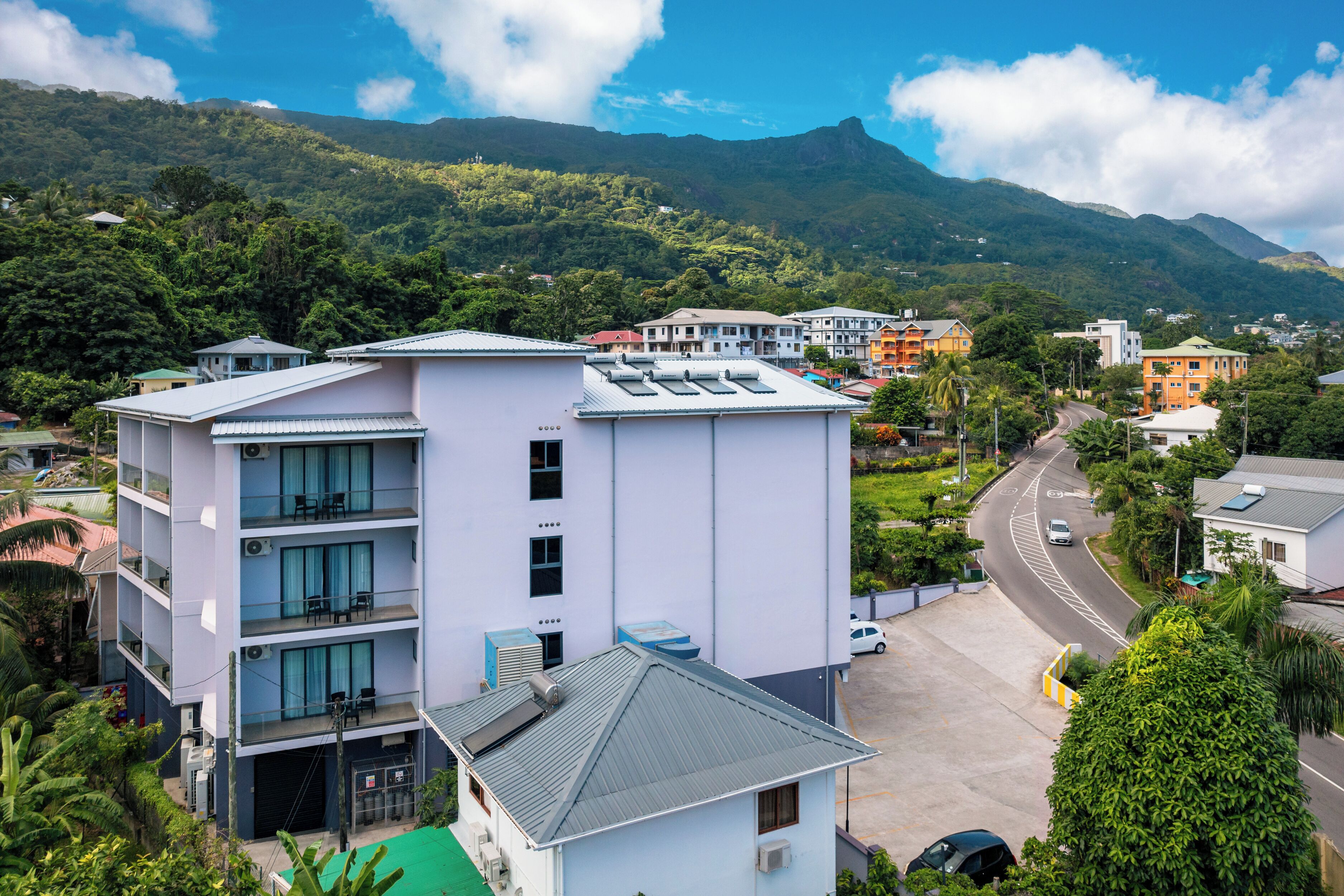 Un hôtel à plusieurs étages doté de balcons, d’un parking et offrant une vue sur la verdure environnante et les montagnes.