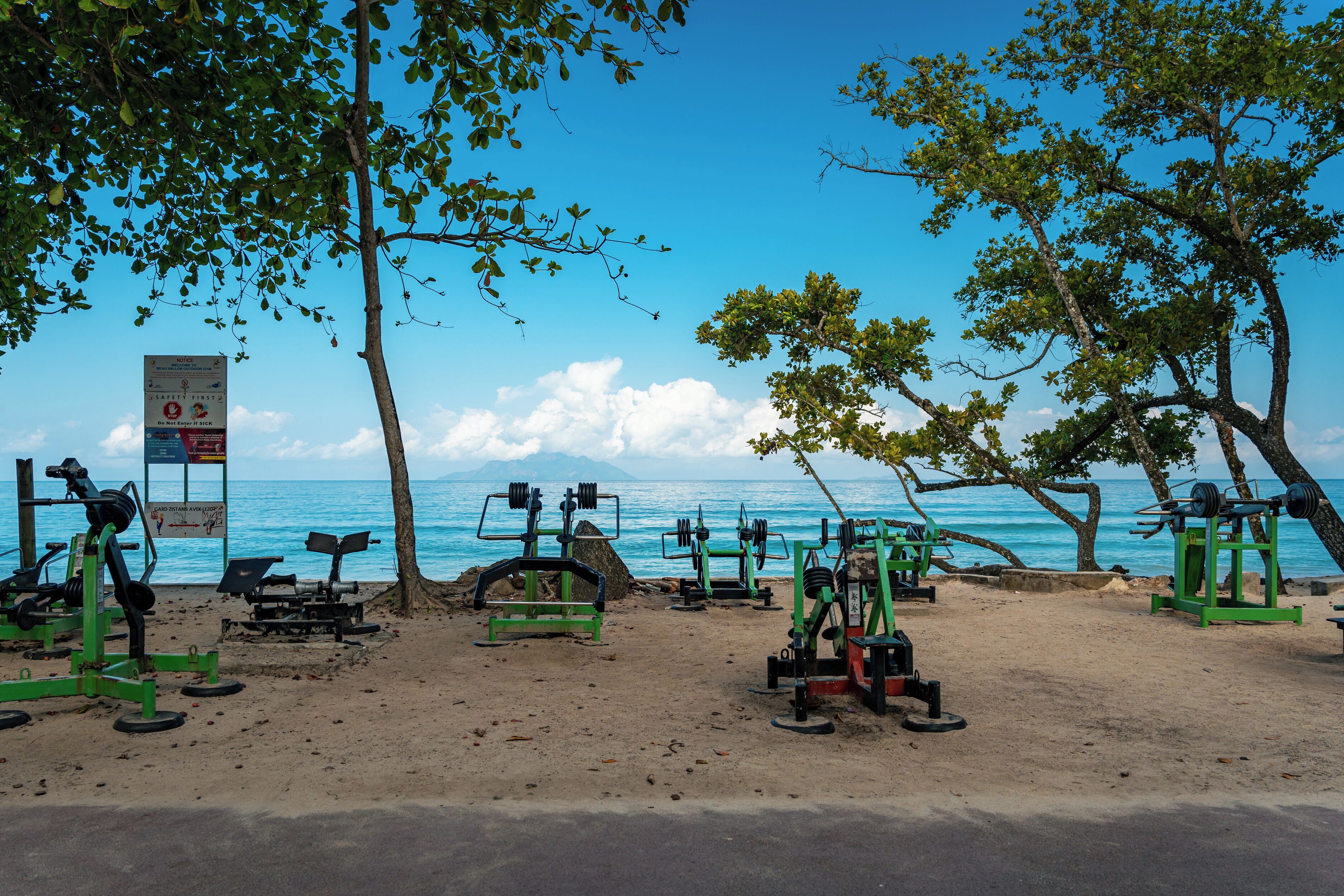 A beachside gym with exercise equipment and a signboard.