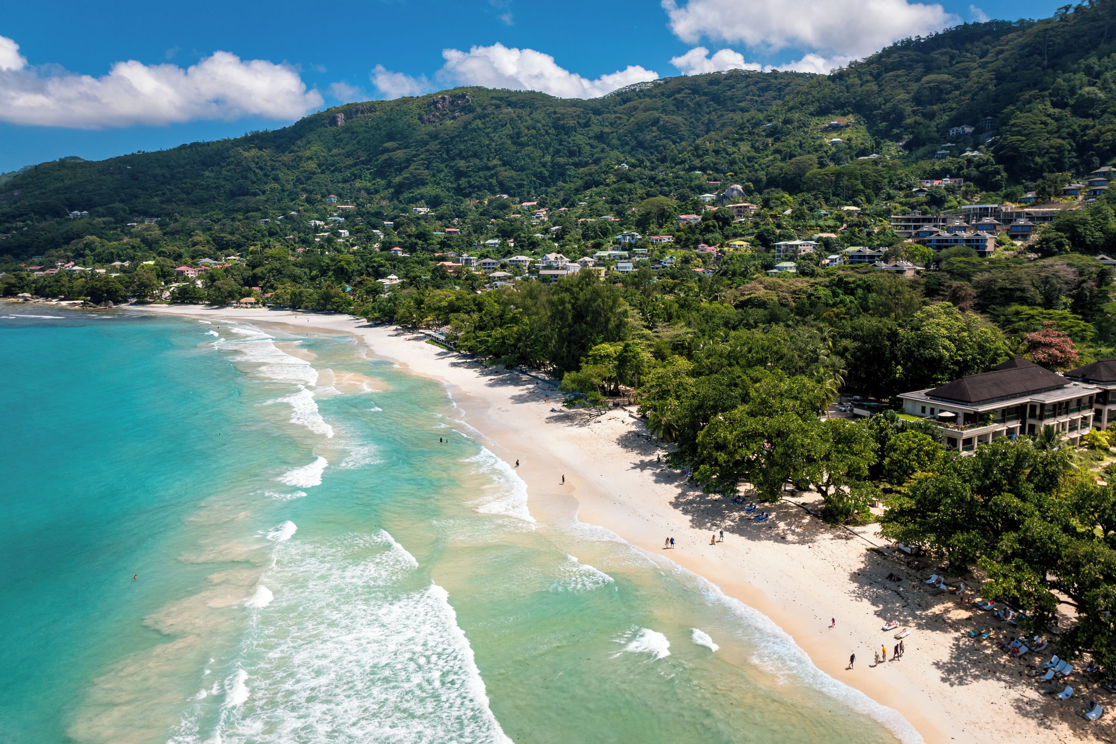 A coastal resort with beachfront properties, lush greenery, and a mountainous backdrop.