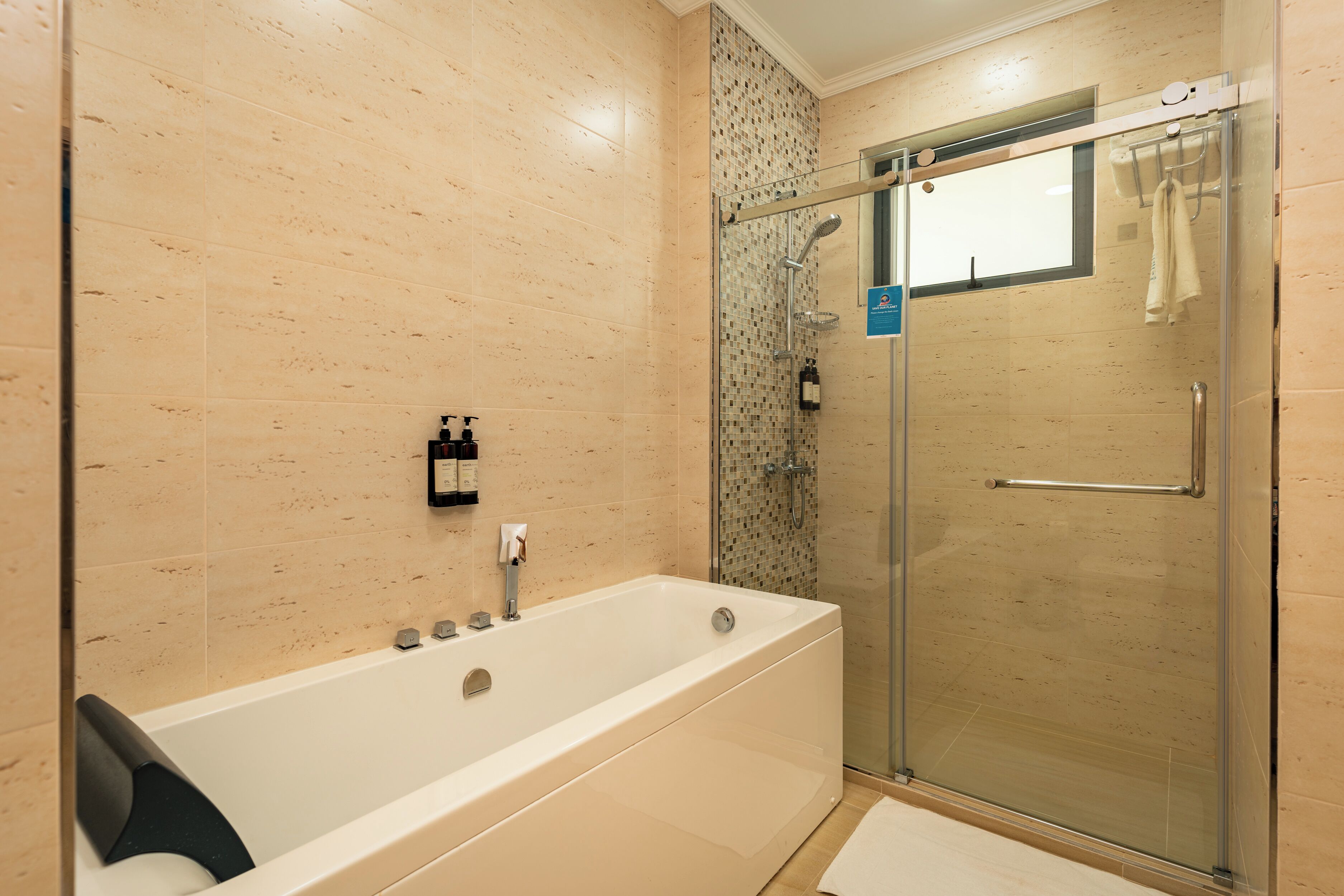 A modern bathroom with a glass-enclosed shower, a white bathtub, and beige tiled walls.