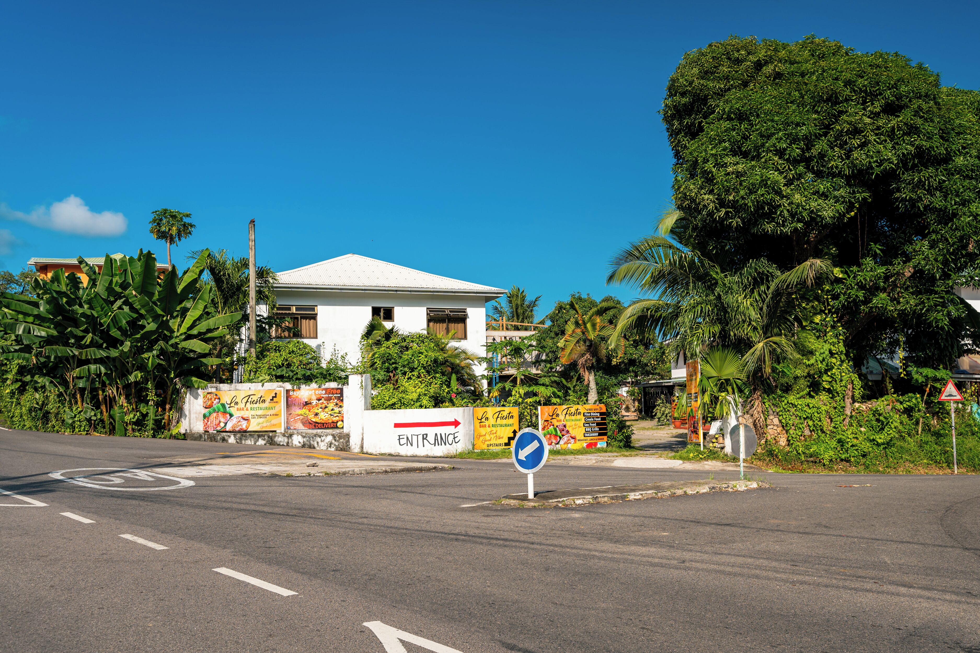 A white building with a sign indicating an entrance, surrounded by lush greenery and palm trees.