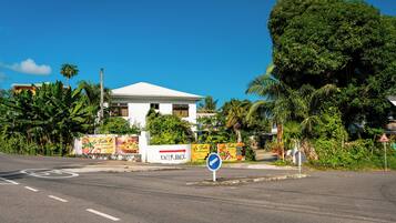 A white building with a sign indicating an entrance, surrounded by lush greenery and palm trees.