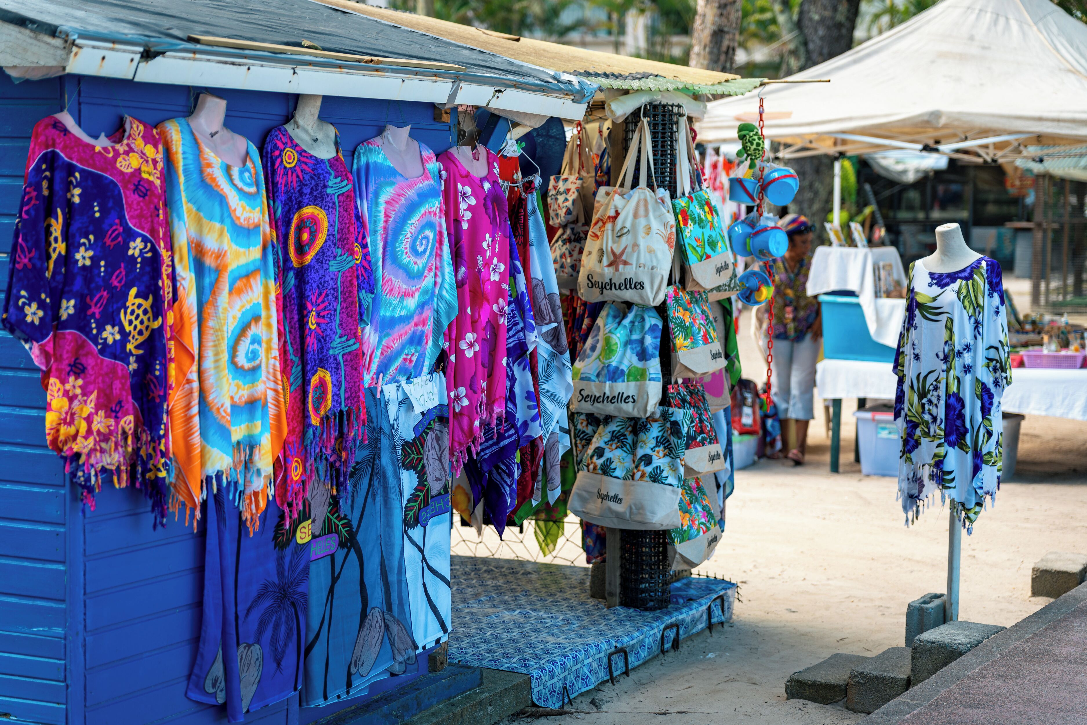 A stall with colorful fabrics and bags, a blue building, and a table with a white tablecloth.