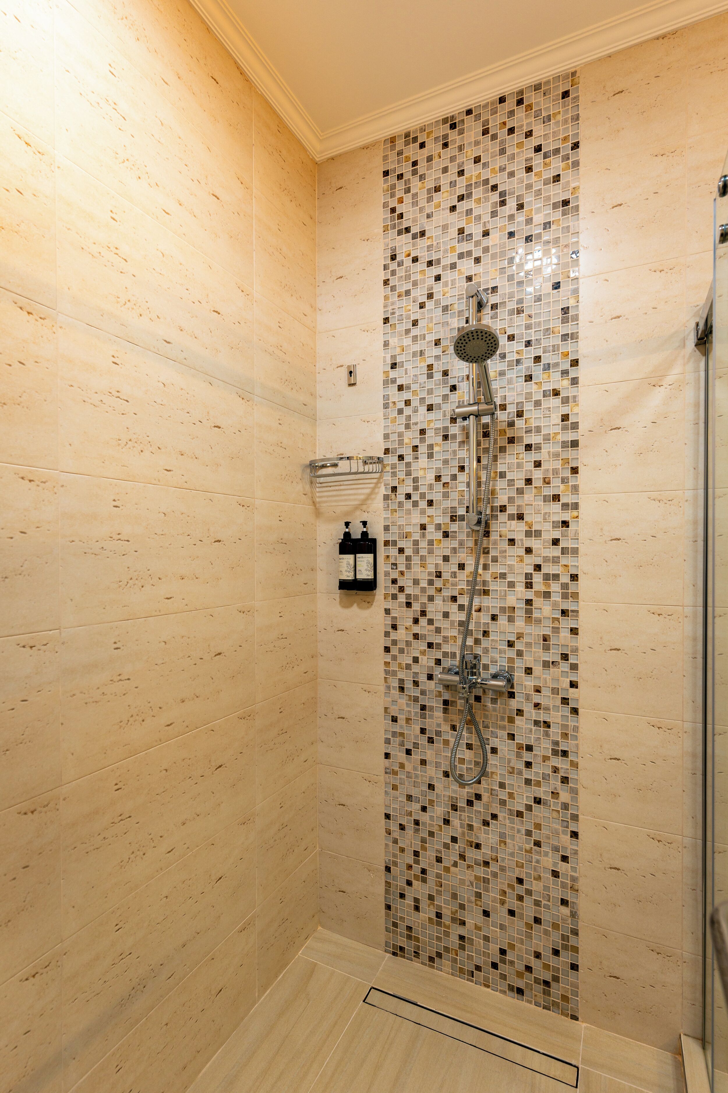 A shower with a tiled wall, a handheld showerhead, and a glass-enclosed shower area.