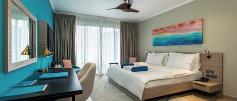 A modern hotel room with a large bed, a desk, a chair, a desk lamp, and a ceiling fan.