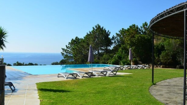 Área da piscina com espreguiçadeiras, um espaço de estar coberto e vista para o mar.
