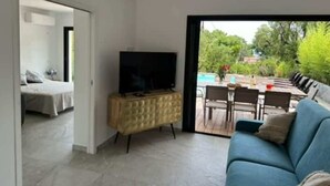 Una sala de estar moderna con un televisor sobre un mueble de madera, un sofá azul y un comedor con asientos exteriores.